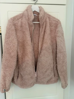 Teddyjacka  - Supermjuk teddyjacka i ljusrosa från Primark. Jackan har hög krage, dragkedja framtill och två fickor. Perfekt för att hålla värmen under kyliga dagar. Tillverkad i fluffigt material som ger en mysig look.