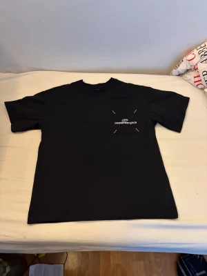  Maison Margiela t-shirt - Säljer  t-shirt från Maison Margiela med en unik bröstficka där loggan är tryckt upp och ner. T-shirten har korta ärmar och en klassisk passform. Perfekt för dig som gillar minimalistisk design med en twist.