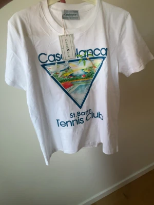 Vit Casablanca Tennis Club t-shirt - Snygg vit t-shirt från Casablanca med färgglatt tryck på bröstet och texten 'St. Barth Tennis Club'. Klassisk passform och rund hals. Perfekt för dig som gillar sportig och trendig stil.
