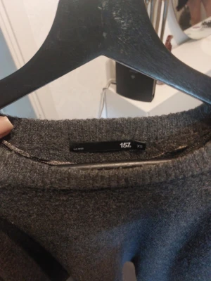 Mörkgrå stickad tröja 157 XS - Mysig mörkgrå stickad tröja från 157 i storlek XS. Tröjan har en avslappnad passform, rund halsringning och trekvartsärmar. Perfekt för lager på lager och enkel att matcha med olika outfits.Passar even S,M