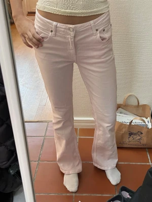 Ljusrosa lågmidjade bootcut jeans - Säljer ett par ljusrosa jeans med bootcut passform. Jag är 173 cm. Jeansen har hög midja och stängs med knapp och ndragkedja. Materialet är mjukt och stretchigt, vilket gör dem bekväma att bära hela dagen.