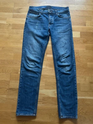Nudie Jeans Solid Ollie W32/L34 - Säljer ett par Nudie Jeans Solid Ollie i storlek W32/L34. Fint använt skick med naturligt slitage. Mindre slitage på ena bakfickan (syns på bild). Nytvättade och redo att användas.