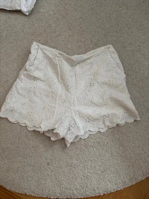 Vita broderade shorts från Zara - Säljer ett par vita shorts från Zara med broderade blommor och vågig kant. Supersöta detaljer och fickor på sidorna.