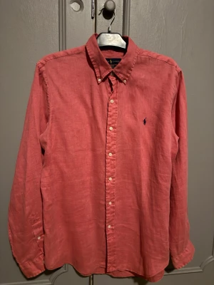 Rosa linneskjorta från Ralph Lauren - Snygg rosa skjorta i linne med klassisk krage och knäppning framtill. Långärmad modell med diskret broderad logga på bröstet. Perfekt för en avslappnad men stilren look.