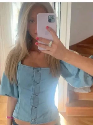 Ljusblå offshoulder jeansblus - Trendig ljusblå jeansblus med offshoulder-modell och puffiga trekvartsärmar. Blusen har knappar framtill och en smickrande figurnära passform. Tillverkad i mjukt denimtyg som ger en cool och avslappnad vibe. Köpt här på plick och endast använd fåtal gånger av mig💕
