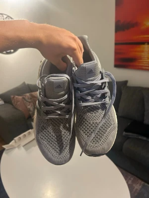 Grå Adidas Ultra Boost sneakers - Snygga grå Adidas Ultra Boost sneakers med stickad ovandel i mesh för bra andningsförmåga. Skorna har vita Boost-sulor och klassiska tre ränder på sidan. Perfekta för dig som gillar stilrena och bekväma sneakers.