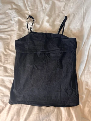 Svart linnetopp med smala axelband - Snygg svart linnetopp med tunna axelband och enkel, rak passform. Toppen är ärmlös och har en stilren look som passar till många olika outfits. Tillverkad i ett lätt och bekvämt material, perfekt för varma dagar.