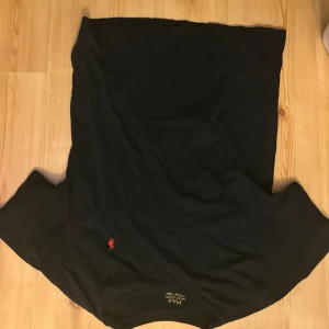 Svart t-shirt från Polo Ralph Lauren - Svart t-shirt från Polo Ralph Lauren med klassisk röd broderad logga på bröstet. T-shirten har rund halsringning och är tillverkad i mjukt bomullsmaterial. Enkel och stilren design som passar till det mesta.