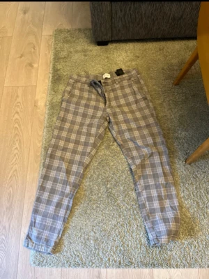 Lindbergh chinos  - Snygga chinos med rutigt mönster i beige och grå toner. Byxorna har normal passform, snedställda fickor fram och en bakficka med knapp. Perfekta för dig som vill ha en stilren men avslappnad look.
