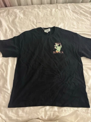 Svart t-shirt från Casablanca - Säljer en svart t-shirt från Casablanca med tryck av en kaktus och blommor samt texten 'Casa Blanca' på bröstet. T-shirten har rund hals och korta ärmar. Perfekt för dig som gillar stilrena plagg med en twist.