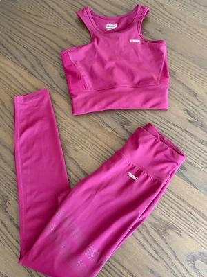Rosa träningsset från Stronger - träningsset från Stronger med sport-bh och tights. Setet är gjort i ett stretchigt funktionsmaterial som andas och har logga på både bh och byxa. Stronger-loggan på byxorna är slitet men annars i bra skick. Färgen är mörkare i verkligheten än vad den ser ut på bilderna. 
