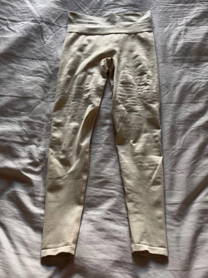 Beige ribbade leggings från Gavelo - Säljer ett par stilrena beige leggings med ribbad struktur och medel hög midja. De är bra längd i modellen och har en mjuk, stretchig passform som sitter snyggt. Är väldigt sköna att både träna i men även att bara gå runt i. 