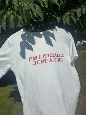 Vit t-shirt med röd text ”I’m litterally just a girl” - Vit t-shirt i bomull med trycket 'I'M LITERALLY JUST A GIRL' i rött framtill. Klassisk rund halsringning och korta ärmar. Aldrig använd endast upptagen ut påse.