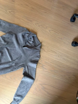 Grå stickad tröja med half zip - Snygg grå stickad tröja med half zip och hög krage. Tröjan har långa ärmar och en liten broderad logga på bröstet. Perfekt för lager på lager och enkel att matcha med jeans eller kjol.100 procent cashmir,knappt användt den 
