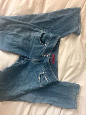 Blå raka jeans från Levis  - Säljer ett par klassiska blå jeans från Levis  med raka ben och dubbla knappar i midjan. Jeansen har fem fickor och tydliga sömmar som ger en snygg vintagekänsla. Perfekta för dig som gillar en avslappnad men trendig stil. Det är rosa sömmar! Raka i benen, inte alls skinny asså
