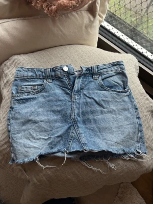 Ljusblå jeanskjol med fransig kant från bershka - Säljer en ljusblå jeanskjol i kort modell med rå, fransig kant nertill. Kjolen har klassiska fem fickor, bälteshällor och knappstängning framtill. Perfekt för dig som gillar en avslappnad och trendig denimlook.