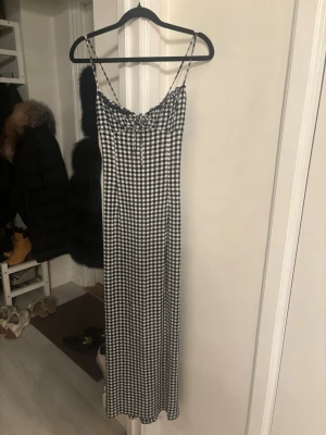 Ny viral Zara klänning  - Långklänning med smala axelband och svartvitt rutigt mönster. Klänningen har en figurnära passform upptill och faller rakt ner. Perfekt för sommardagar och har en enkel men trendig look.