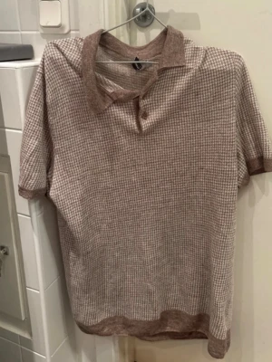 Beige henley från Gran Sasso - Snygg beige henley från Gran Sasso med diskret rutigt mönster och klassisk krage. Skjortan har knappar vid halsen och är tillverkad i mjukt material som känns lyxigt mot huden. Perfekt för dig som gillar stilrena och tidlösa plagg.