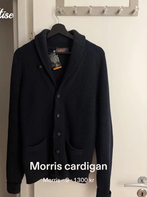 Mörkblå stickad cardigan från Morris - Säljer en mörkblå stickad cardigan från Morris med grov ribbad struktur. Koftan har knappar framtill, två fickor och en snygg krage. Perfekt för lager på lager och en klassisk look.