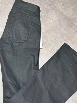 Svarta utsvängda skinnbyxor/ jeans - (Står storlek M men sitter mer som S.)Snygga svarta jeans med utsvängda ben och klassisk femficksdesign. Jeansen har låg midja och raka sömmar längs benen. Materialet är skinn/läder. Står storlek M men sitter mer som S.