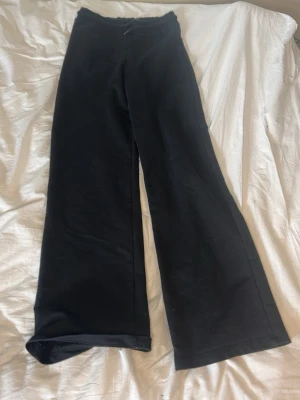 Svarta vida leggings - Säljer ett par svarta leggings med hög midja och vida ben. De har en enkel och stilren design utan synliga detaljer eller loggor. Materialet ser mjukt och stretchigt ut, perfekt för en avslappnad look.