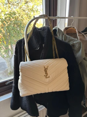 Vit handväska från YSL loulou - Säljer en snygg vit quiltad handväska från YSL med guldiga kedjehandtag och ikonisk YSL-logga framtill. Den är i läder💞 inte mycket använd varav varför jag säljer den. Mått är följande, 21 cm höjd och 31 cm beredd. 🎀 