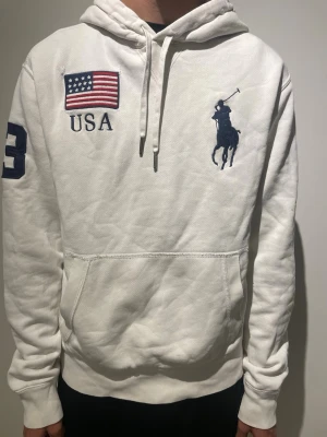 Ralph Lauren hoodie  - Fet Vit Ralph lauren hoodie, den har inga smutsiga fläckar men har fått lite skador vid de amerikanska flaggorna fram och bak. Modellen är 178cm 