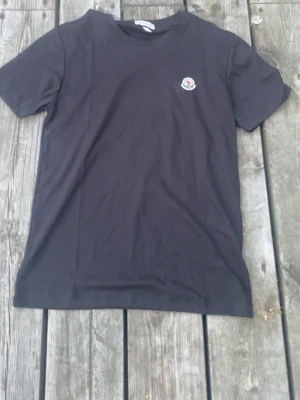 Svart t-shirt från Moncler - Snygg svart t-shirt från Moncler med klassisk rund hals och Moncler-logga broderad på bröstet. Enkel och stilren design som passar till det mesta. Tillverkad i mjuk bomull för skön känsla.