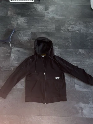 Ea7 zip up  - Svart EA7 Hoodie i storlek M. Passar perfekt till dig som vill är en enkel och simpel person. Perfekt för en chill dag. Mitt pris 300