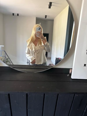Beige blus med volangdetaljer - En beige blus med volanger. Den går att knäppa upp hela vägen till halsen. 