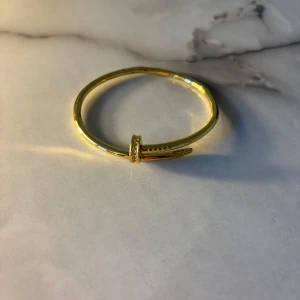 Guldigt armband - Snyggt armband i guldton med unik spikformad design. Armbandet har glittriga stenar på toppen som ger extra bling. Perfekt accessoar för dig som vill sticka ut och addera lite edge till din stil.