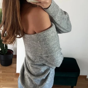 Grå off shoulder stickad tröja - Trendig grå stickad tröja med off shoulder-design och bred ribbad kant upptill. Mjuk och skön, perfekt för lager på lager. Långa ärmar och avslappnad passform ger en chill vibe. Passar perfekt till jeans eller kjol.