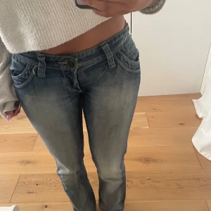 Blå bootcut jeans med dragkedjor - Säljer ett par blå bootcut jeans från indian rose med snygga slitningar och dragkedjor på bakfickorna. Jeansen har låg midja och klassisk femficksdesign. Perfekta för dig som gillar en avslappnad men ändå trendig look. Midjemått 36 cm 88 cm långa. Har sytt in dom lite. 