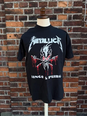Metallica Vintage T-shirt – Binge & Purge – Summer Shit 1994 World Tour – XL - Vintage Metallica Binge & Purge Summer Shit 1994 World Tour T-shirt i XL. Stort tryck fram och stort turnétryck bak med Danzig & Suicidal Tendencies. 100 % bomull. Mycket fint vintageskick med skarpa tryck och djup svart färg. Etiketten är delvis bortklippt, se bilder. En ovanlig och eftertraktad Metallica-tröja från 90-talet som sällan dyker upp i detta skick. 