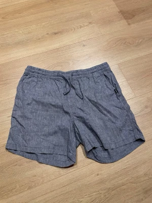 Mörkgrå shorts från Jack & Jones - Säljer ett par mörkgrå shorts från Jack & Jones med snörning i midjan och avslappnad passform. Shortsen har sidofickor och är tillverkade i ett mjukt bomullsmaterial, perfekta för varma dagar.