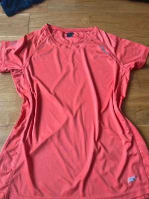 Korallrosa tränings-tshirt - Snygg korallrosa tränings-tshirt i funktionsmaterial. T-shirten har korta ärmar, rund halsringning och är lätt figursydd för en sportig look. Perfekt för löpning, gym eller annan träning.