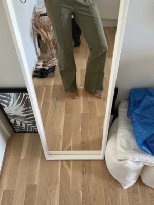 Olivgröna bootcut jeans - Säljer ett par olivgröna jeans med bootcut-modell och markerade sömmar framtill. Jeansen har fickor med knappdetaljer och hög midja. Snygga att styla med både sneakers och boots. Materialet är kraftigt och stretchigt för skön passform.