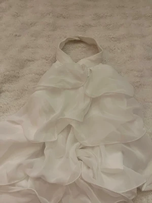 Vit volangklänning från SHEIN - Säljer en vit kortklänning från SHEIN med halterneck och flera lager av volanger. Klänningen är ärmlös och har en luftig, flowy känsla som ger en romantisk look. Perfekt för sommarens alla tillfällen!