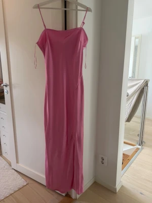 Rosa klänning - Säljer en enkel och stilren rosa långklänning med smala axelband och rak passform. Klänningen har en mjuk, slät yta och är perfekt för varma dagar. Passar dig som gillar minimalistisk och feminin stil.