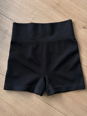 Svarta ribbade cykelshorts - Snygga svarta ribbade träningsshorts med hög midja och scrunch baktill som ger en smickrande passform. Stretchigt och bekvämt material, perfekta till gymmet, promenader eller vardags. Storlek S. Fint skick.