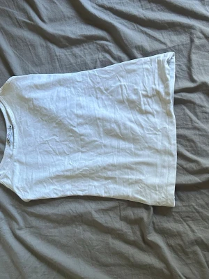 Vit basic t-shirt i bomull - Enkel vit t-shirt i mjuk bomull med rund hals och korta ärmar. Perfekt till jeans eller shorts för en clean och avslappnad look. Klassisk passform och lätt material som funkar året runt.