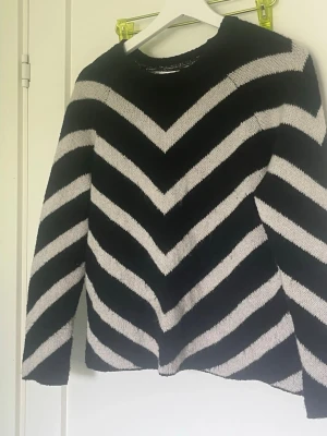 Svartvit stickad tröja med zigzag-mönster - Säljer en svart stickad tröja med breda vita zigzag-ränder. Tröjan har rund halsringning och långa ärmar. Materialet känns mjukt och stretchigt, perfekt för dig som gillar en avslappnad men ändå trendig look.
