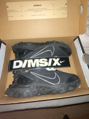 Svarta Nike D/MS/X sneakers - Säljer ett par svarta Nike D/MS/X sneakers med chunky sula och tydlig vit swoosh på sidan. Skorna har en unik, vågig sula och meshmaterial på ovandelen för extra ventilation. Perfekta för dig som gillar streetwear och vill sticka ut.
