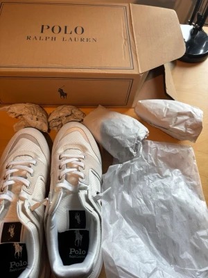 Vita sneakers från Polo Ralph Lauren - Snygga vita sneakers från Polo Ralph Lauren med klassisk låg profil. Skorna har ovandel i mesh och syntet med detaljer i läderimitation, vita snören och svart yttersula. Perfekta för en clean och stilren look.