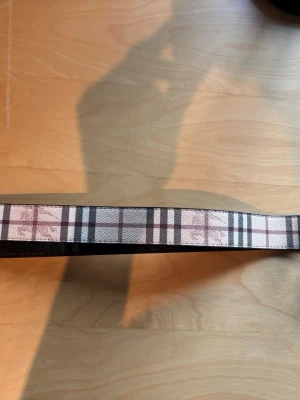 Burberry bälte  - Du får med allt som syns på bild 3 för ett riktigt schysst pris!! Snyggt bälte med klassiskt rutigt mönster i svart, vitt och beige. Bältet är gjort i skinn och har flera hål för justering. Perfekt accessoar för att lyfta din outfit. 
