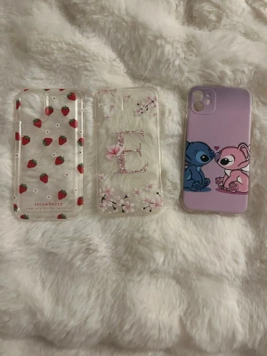 3 snygga mobilskal med olika motiv - Säljer tre mobilskal: ett genomskinligt med jordgubbar, ett transparent med blommor och bokstaven E i mitten, samt ett lila skal med Stitch och Angel från Lilo & Stitch. Alla skal är i mjukt plastmaterial och har unika, färgglada designer som sticker ut. 65kr för alla skal priset kan diskuteras om någon bara villa ha ett skal. Skalen är aldrig andvända och till en iPhone 11