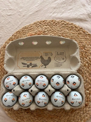 Golfbollar TaylorMade pix 10 - Säljer ett set med 10 vita golfbollar från TaylorMade, snyggt förpackade  Bollarna har svart och orange mönster samt TaylorMade-logga tryckt på varje boll. Perfekt för dig som vill ha unika golfbollar till nästa runda. Pix bollar a klass