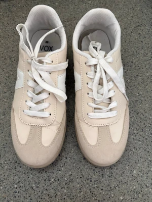 Beige och vita sneakers från VOX - Snygga sneakers i beige och vitt från VOX. Skorna har klassisk låg modell med vita snören, detaljer i mockaimitation och paneler i syntetläder. Sidan pryds av en vit rand och insidan är vadderad för extra komfort. Kolla gärna mina andra annonser❗️