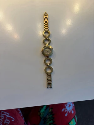 Guldig DKNY armbandsklocka i metall - Snygg armbandsklocka från DKNY i guldigt metallutförande. Klockan har ett unikt armband med stora cirkelformade länkar och en rund urtavla med minimalistisk design. Perfekt accessoar för att lyfta din outfit. Fungerar inte, kan diskutera pris 