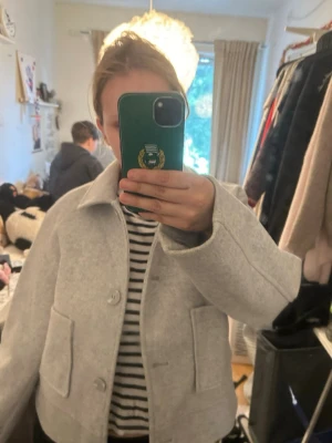 Ljusgrå  jacka med knappar - Snygg ljusgrå jacka i oversized modell med stora fickor framtill och knäppning med stora knappar. Jackan har klassisk krage och raka, långa ärmar. Perfekt för dig som gillar minimalistisk och clean stil.
